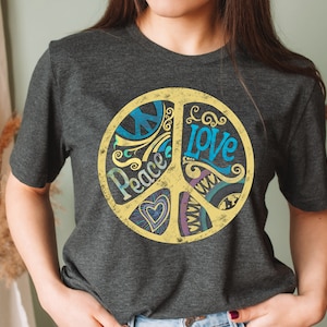 Op de afbeelding: Een donkergrijs T-shirt met een gele peace-teken graphic. Het peace-teken is versierd met blauwe, paarse en groene swirls en de woorden "Peace" en "Love" zijn in het teken geschreven.