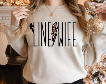 May include: A cream-colored sweatshirt with the text "LINE WIFE" in black lettering. A leopard print lightning bolt graphic is centered between the words.