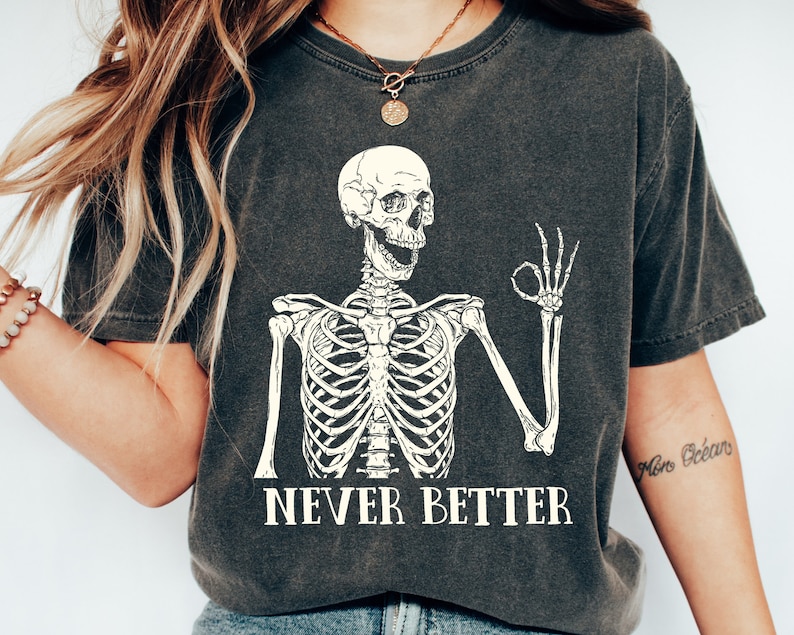 May include: A dark gray t-shirt with a white skeleton graphic giving the OK sign. The text "NEVER BETTER" is printed below the skeleton.