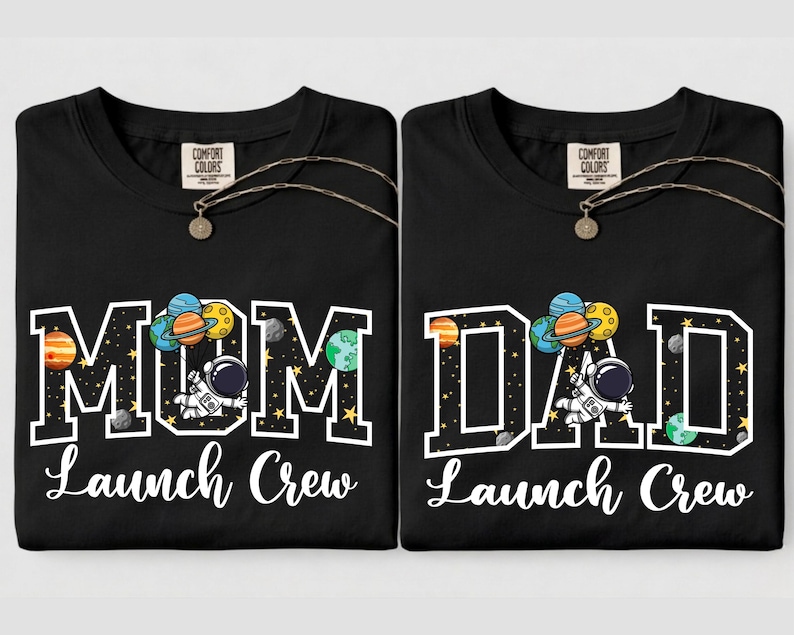 Puede incluir: Dos camisetas negras con las palabras "MOM Launch Crew" y "DAD Launch Crew" en blanco. Cada camiseta presenta un gr&aacute;fico tem&aacute;tico espacial con planetas, un astronauta y la etiqueta Comfort Colors.