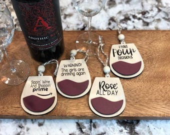 May include: Four wooden wine glass ornaments with different sayings. The sayings are "Sippin' Wine And Shoppin' prime", "WARNING! The girls are drinking again", "I Make Pour Decisions", and "Rose' All Day".
