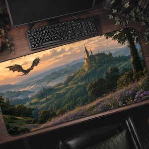 May include: A rectangular desk mat featuring a printed landscape illustration of a large stone castle perched on a green hillside at sunset, with a dark dragon flying in the sky and a foreground filled with purple wildflowers and lush green trees.