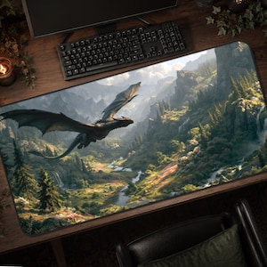 May include: A rectangular desk mat featuring a detailed illustration of a dark dragon in flight over a lush mountain valley with evergreen trees, rocky cliffs, and a winding river flowing through the landscape under a cloudy sky.