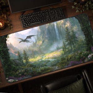 May include: A rectangular desk mat featuring a detailed fantasy landscape illustration. The scene depicts a flying dragon soaring over a lush valley with a tall waterfall, evergreen trees, rocky cliffs, and a vibrant meadow filled with colourful flowers.