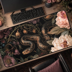 May include: A rectangular desk mat featuring a dark black background with a detailed illustration of a coiled snake surrounded by large, blooming pink and white peonies, green foliage, and small hanging bell-shaped flowers in muted purple tones.