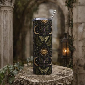 Könnte beinhalten: Ein hoher zylindrischer Becher mit transparentem Deckel und Metallstrohhalm. Die Außenseite zeigt ein dunkles Muster aus goldenen Sonnen, Mondsicheln, grünen Nachtfaltern, Farnen und violetten Kristallen in einem botanischen Design.