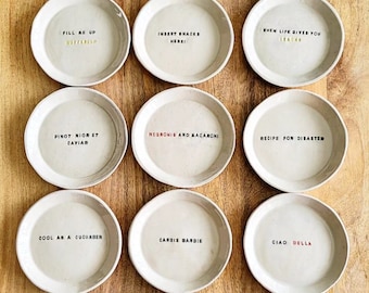 Può includere: Dodici sottobicchieri in ceramica bianca con lettere dorate. Ogni sottobicchiere ha un detto divertente diverso. I detti includono "Snack Surfing", "Dessert First", "Good Food 3000 5000", "Fill Me Up", "Insert Snacks Here", "When Life Gives You Leadus", "Pinot Noir Et Cavier", "Negronis and Macaroni", "Recipe for Disaster", "Cool as a Cucumber", "Cardie Bardie", "Ciao Bella", "Who Said I Can't Cook?", "Soup of the Day: Champaigne", and "Good Times and Sunshine".