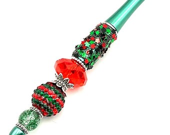 May include: A green pen with red and green glitter and beads. The pen has a silver cap and a red and green crystal bead.