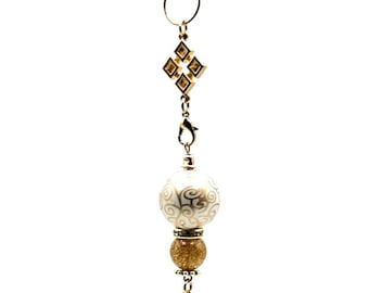 Op de afbeelding: Een gouden kerstversiering met een witte sneeuwvlok charme, een gouden glitterkraal en een witte kraal met gouden swirls. De versiering is bevestigd aan een gouden haak.