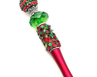 May include: A red pen with a green and red beaded top. The beads are decorated with rhinestones and glitter.