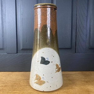 May include: A ceramic vase with a tall, tapered design. The top is brown, fading into olive green, and then to a white base. The white base has painted butterfly designs in brown and black. A decorative home accent.