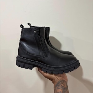 May include: A pair of black ankle boots featuring a smooth matte finish, a side zip closure, a pull tab at the heel, and a thick, chunky lug sole. The boots have a rounded toe design and a reinforced metal rivet detail near the top zip area.