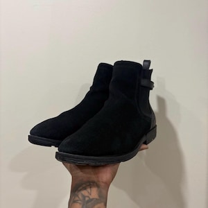 Peut inclure: Une paire de bottines noires avec une tige en suédine, un bout arrondi, un petit talon et une bride décorative près du col. Les bottines sont dotées d'une languette à l'arrière et d'une semelle en caoutchouc noir texturé pour l'adhérence.