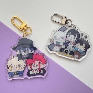 May include: A set of two acrylic keychains featuring cartoon characters. The first keychain features four characters with a camera and the text "LINK CLICK". The second keychain features three characters with black, red, and blue clothing.