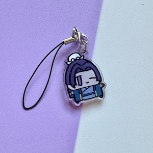 May include: A clear acrylic charm featuring a cartoon character with dark blue hair and clothing. The charm has a black lanyard and a silver-colored clasp. The background is a split of purple and white.
