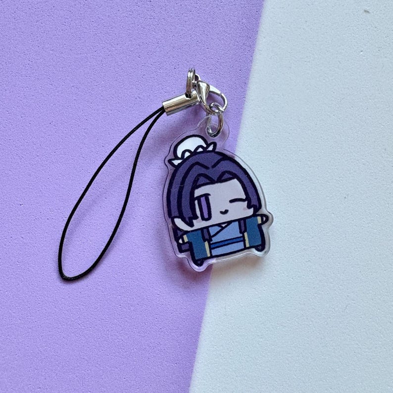 May include: A clear acrylic charm featuring a cartoon character with dark blue hair and clothing. The charm has a black lanyard and a silver-colored clasp. The background is a split of purple and white.