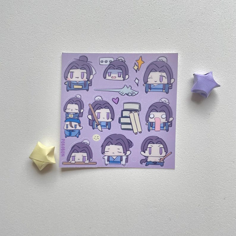 May include: A sheet of stickers featuring cartoon characters with purple hair and blue outfits. The stickers have various poses and expressions. The sheet is on a white surface, with two origami stars in yellow and purple.