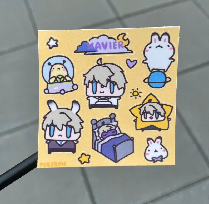 Op de afbeelding: Een set gele, witte en blauwe stickers met een cartoonfiguur genaamd "Xavier". De stickers bevatten een figuur in een ruimteschip, een figuur die slaapt in een bed, een figuur in een ster en een konijn.