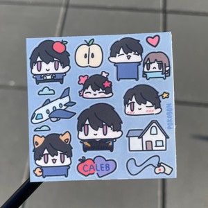 Op de afbeelding: Een vel met stickers met cartoonfiguren met verschillende gezichtsuitdrukkingen. De stickers zijn op een lichtblauwe achtergrond met witte wolken, een vliegtuig, een huis en een hart. De tekst "POKOBON" en "CALEB" is zichtbaar op de stickers.