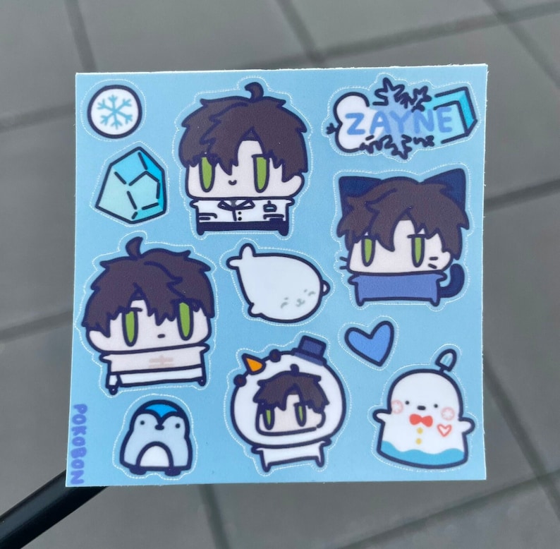 Op de afbeelding: Een vel met blauwe stickers met verschillende cartoonfiguren, waaronder een pingu&iuml;n, een sneeuwpop, een zeehond en een kat. De stickers zijn allemaal in chibi-stijl en hebben een schattige en fantasierijke esthetiek. De tekst "ZAYNE" en "POKOBON" staan ook op het vel.