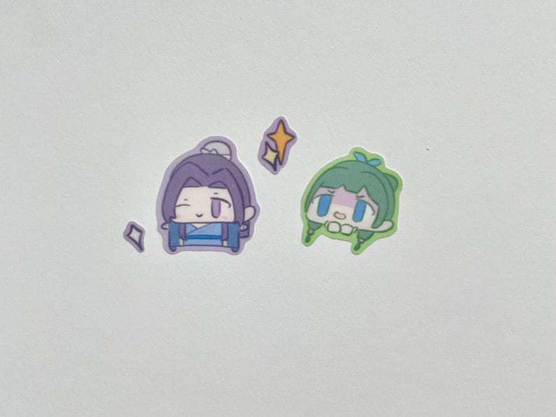 May include: A collection of stickers featuring anime-style characters. One sticker depicts a purple-haired character in blue clothing, while the other shows a green-haired character. Decorative star and diamond shapes are also included.