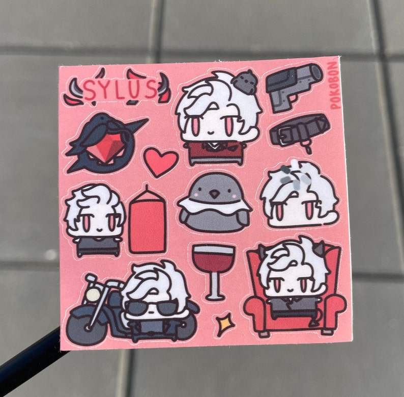 Op de afbeelding: Een roze stickervel met verschillende illustraties van een personage met wit haar en rode ogen. Het personage wordt afgebeeld in verschillende poses en settings, waaronder op een motor rijden, op een troon zitten en een glas wijn vasthouden. Het stickervel bevat ook een hart, een vogel, een kaars en een pistool. De tekst "SYLUS" en "POKOBON" is zichtbaar op het stickervel.