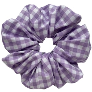 Op de afbeelding: Een grote, gezwollen scrunchie in een ruitpatroon. De stof is lichtpaars en wit, waardoor een klassiek geruit ontwerp ontstaat. De scrunchie is ontworpen om haar vast te houden en is geschikt voor verschillende kapsels.