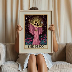 May include: A framed tarot card print featuring a woman in a pink gown holding a disco ball. The artwork has a gold border and the text "THE DISCO" at the bottom. The background is black with stars and a sunburst halo.