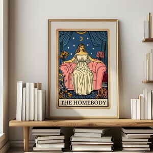 May include: A tarot card illustration with a woman sitting on a pink couch. The card is titled "The Homebody" and features a blue background with stars and a crescent moon.