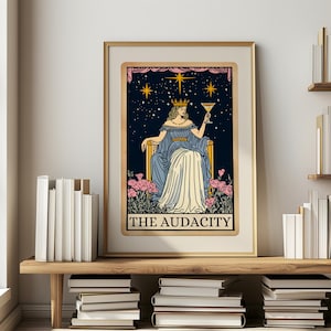 Puede incluir: Impresi&oacute;n art&iacute;stica enmarcada de una carta del tarot que representa una figura con un vestido azul sosteniendo una copa de c&oacute;ctel sobre un fondo de noche estrellada. El texto "THE AUDACITY" est&aacute; en la parte inferior. La obra de arte con marco dorado se exhibe en una estanter&iacute;a de madera con libros.