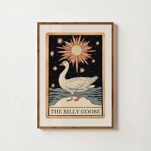 May include: Framed art print with a goose illustration. The image shows a goose on a rock, set against a backdrop of a sun and stars. The text "THE SILLY GOOSE" is at the bottom. The frame is brown.
