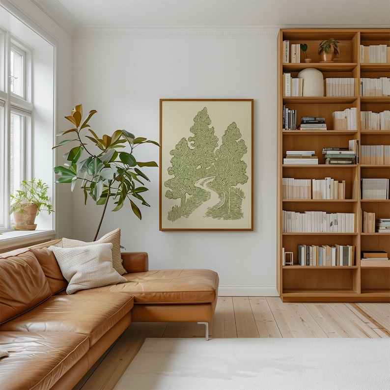 K&ouml;nnte beinhalten: Ein gerahmtes Kunstwerk mit einer gr&uuml;n-wei&szlig;en Illustration von B&auml;umen und einem Pfad. Das Kunstwerk h&auml;ngt an einer wei&szlig;en Wand &uuml;ber einem braunen Ledersofa. Im Hintergrund ist ein gro&szlig;er B&uuml;cherregal aus Holz zu sehen.