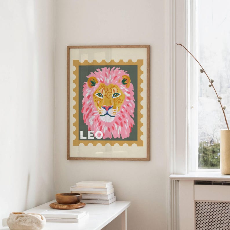 May include: A framed art print featuring a stylized lion's head with a pink mane and yellow face. The word "LEO" is printed in white at the bottom. The artwork is set against a green background with a postage stamp-like border.