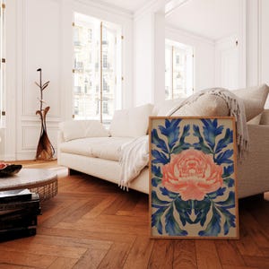 May include: A framed print of a pink flower with blue leaves on a beige background. The print is in a wooden frame and is leaning against a white couch.