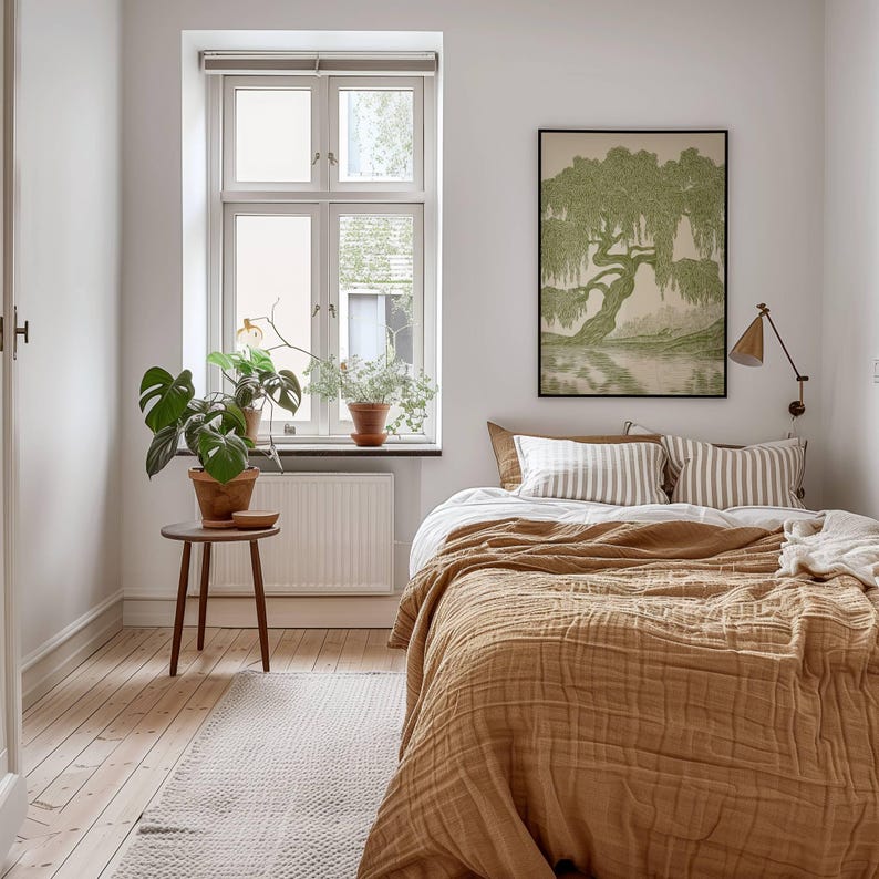 Pu&ograve; includere: Una camera da letto con un letto dotato di una trapunta testurizzata color senape e cuscini a righe, una stampa incorniciata di un salice piangente verde sulla parete, un piccolo tavolino in legno con una pianta monstera e una finestra bianca.