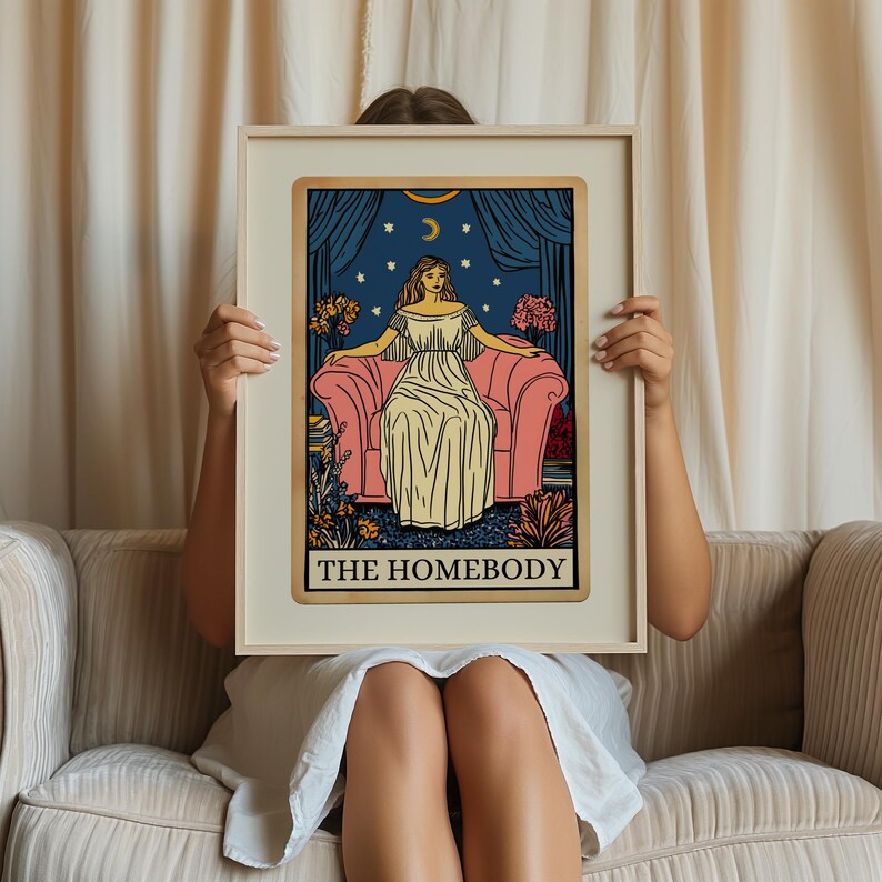 May include: A tarot card with a blue background and gold trim. The card depicts a woman sitting on a pink couch with a starry night sky behind her. The text "THE HOMEBODY" is printed in gold at the bottom of the card.
