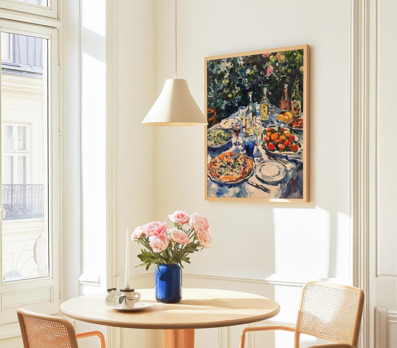 May include: A painting of a table setting with a variety of dishes, including a pizza, fruit, and wine glasses. The painting is framed in a light wood frame and hangs on a white wall.