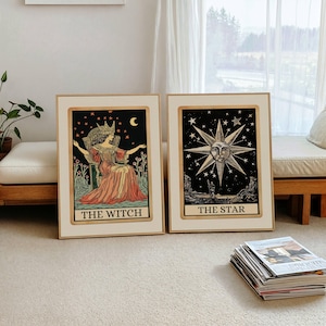 May include: Two framed tarot card prints. One features "THE WITCH" with a woman in a crown, seated under stars and a crescent moon. The other shows "THE STAR" with a sun face surrounded by stars. Both have gold frames.