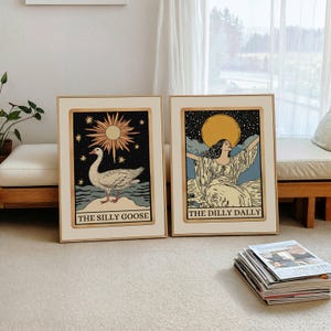 May include: Two framed art prints with light wood frames. One features a goose with the text "THE SILLY GOOSE". The other shows a woman with arms raised and the text "THE DILLY DALLY". Both have a vintage aesthetic with a cream background.