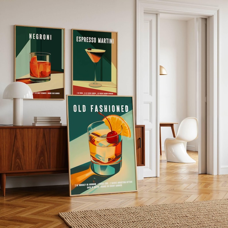 Op de afbeelding: Drie ingelijste kunstprints met cocktailillustraties. De prints tonen een Negroni, Espresso Martini en Old Fashioned. Elke print heeft een teal achtergrond met de cocktailnaam in het wit. De Old Fashioned print bevat een kers en een sinaasappelschijfje als garnering.