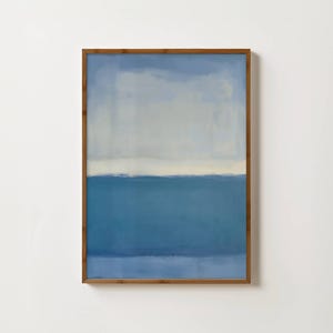 May include: Abstract painting in a wooden frame. The artwork features a gradient of blue hues, with a lighter blue at the top transitioning to a darker blue at the bottom. A horizontal white band divides the colors.