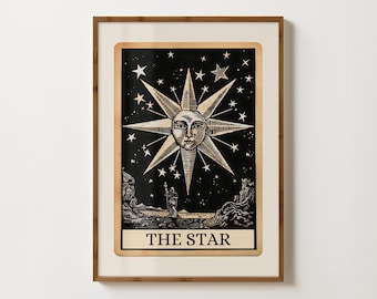 May include: A framed print of a tarot card depicting The Star. The card features a black background with a gold star with a human face in the centre. The star is surrounded by smaller stars.