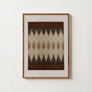 Op de afbeelding: Een ingelijst textielkunstwerk met een herhalend patroon van bruine en zwarte ruitvormen op een beige achtergrond. Het kunstwerk is ingelijst in een lichtbruine houten lijst, wat warmte aan het ontwerp toevoegt.