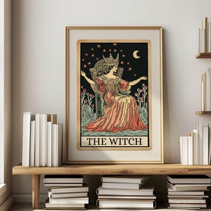 May include: Framed art print of a tarot card titled "The Witch." The illustration features a woman in a crown and gown, seated on a throne against a starry night sky. The artwork is in a gold frame and displayed on a wooden shelf.