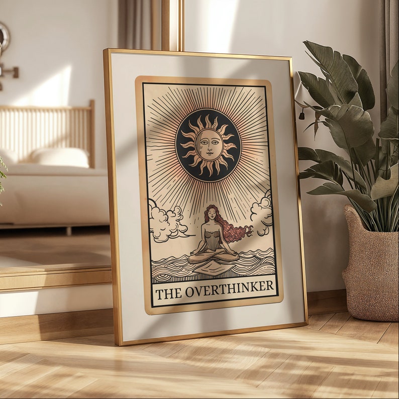 Peut inclure: Une impression encadr&eacute;e dor&eacute;e d'une carte de tarot avec une femme assise en position de lotus sur une &eacute;tendue d'eau. Le soleil brille au-dessus d'elle et la carte indique "The Overthinker".