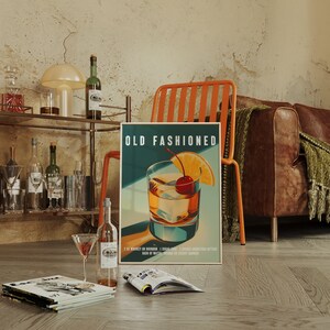 Op de afbeelding: Poster met een "Old Fashioned" cocktail met een kers en sinaasappelschijfje. De poster leunt tegen een oranje stoel, met een leren bank en een barwagen op de achtergrond. Een martiniglas en tijdschriften liggen op de grond.