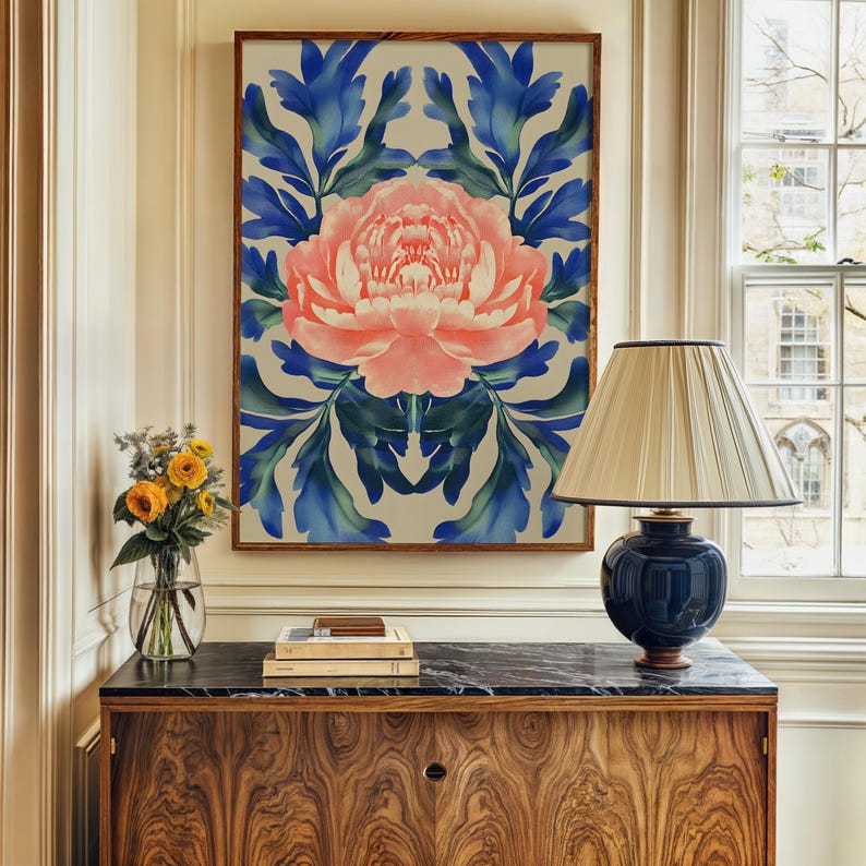 May include: A framed print of a pink peony flower with blue and green leaves on a white background. The print is hanging on a wall above a wooden dresser with a black marble top.