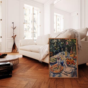May include: A framed watercolor painting depicting a table setting with a pizza, salad, fruit, and wine glasses. The table is set with a blue tablecloth and surrounded by lush greenery.