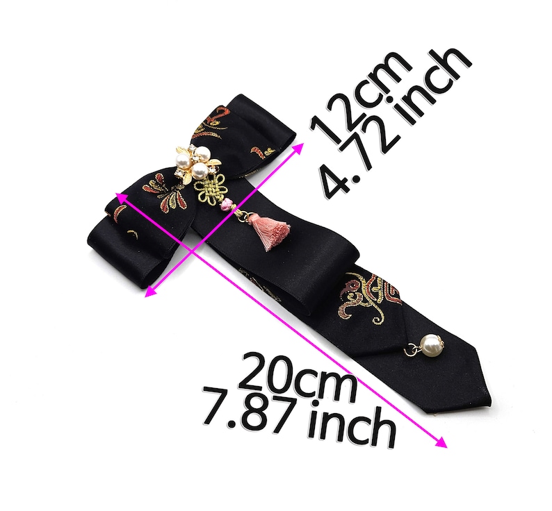 Pode incluir: Gravata borboleta preta com bordado dourado e vermelho, um detalhe de p&eacute;rola e borla, e medidas em cent&iacute;metros: 12 cm por 20 cm.