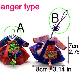 K&ouml;nnte beinhalten: Zwei Miniatur-Hanbok-Ornamente mit Aufh&auml;ngertypen A und B. Das linke Ornament ist blau-rot mit einer gr&uuml;nen Schlaufe, das rechte rosa-blau mit einer violetten Schlaufe. Beide haben Zierknoten und Stickereien. Die Ma&szlig;e betragen 7 cm mal 8 cm.